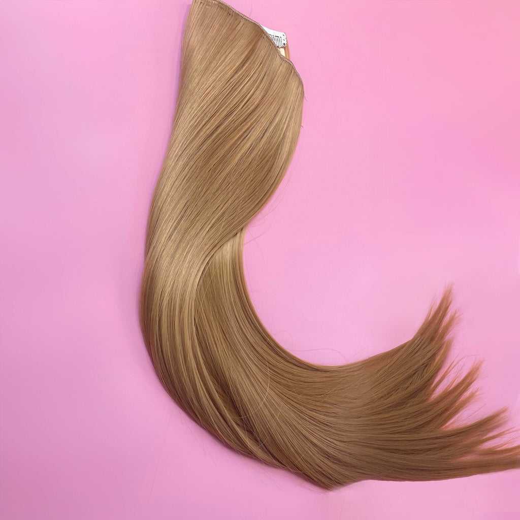 Big Glam Nation 21 inch extensions in sandy brown laid against pink background.