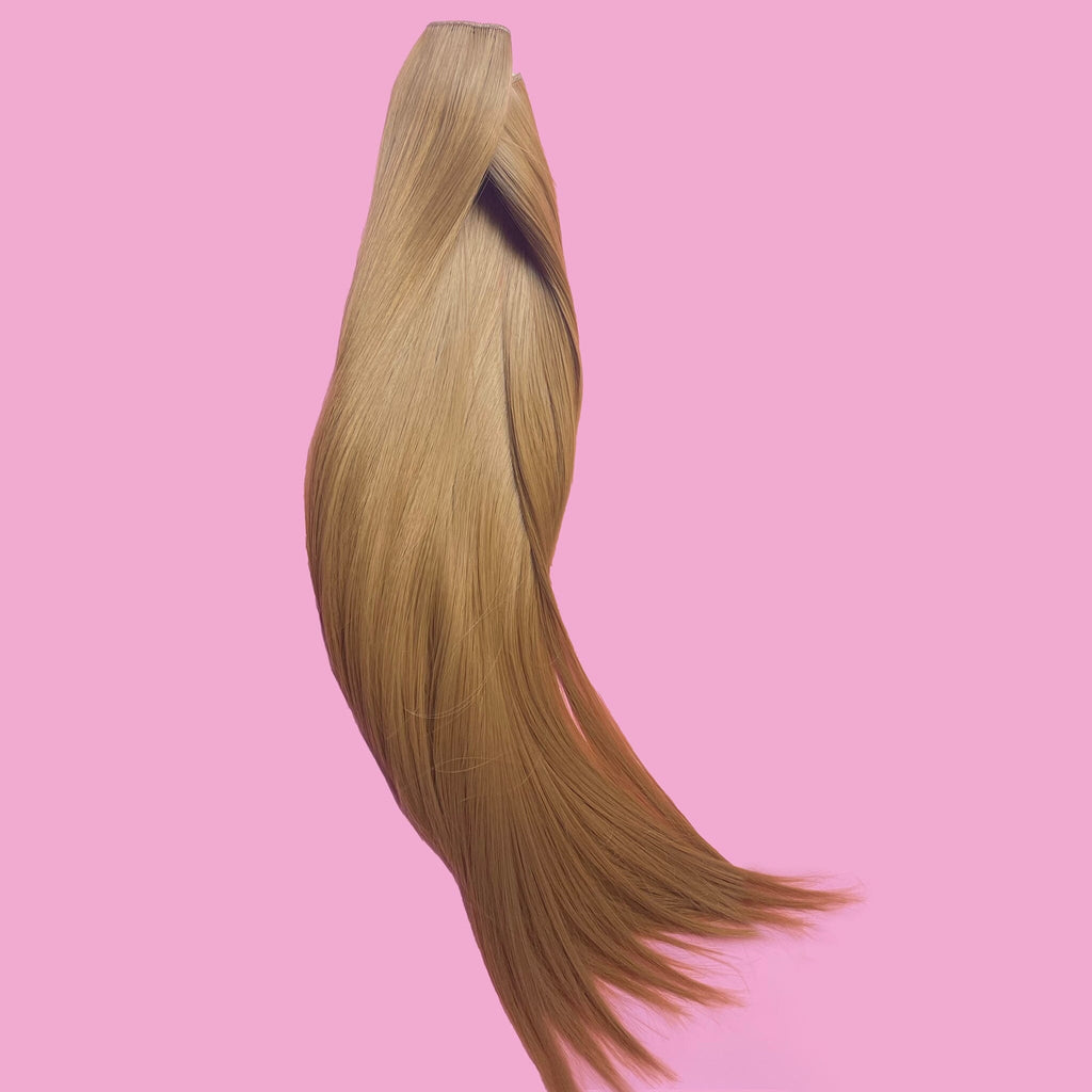 Big Glam Nation 21 inch extensions in sandy brown laid against pink background.