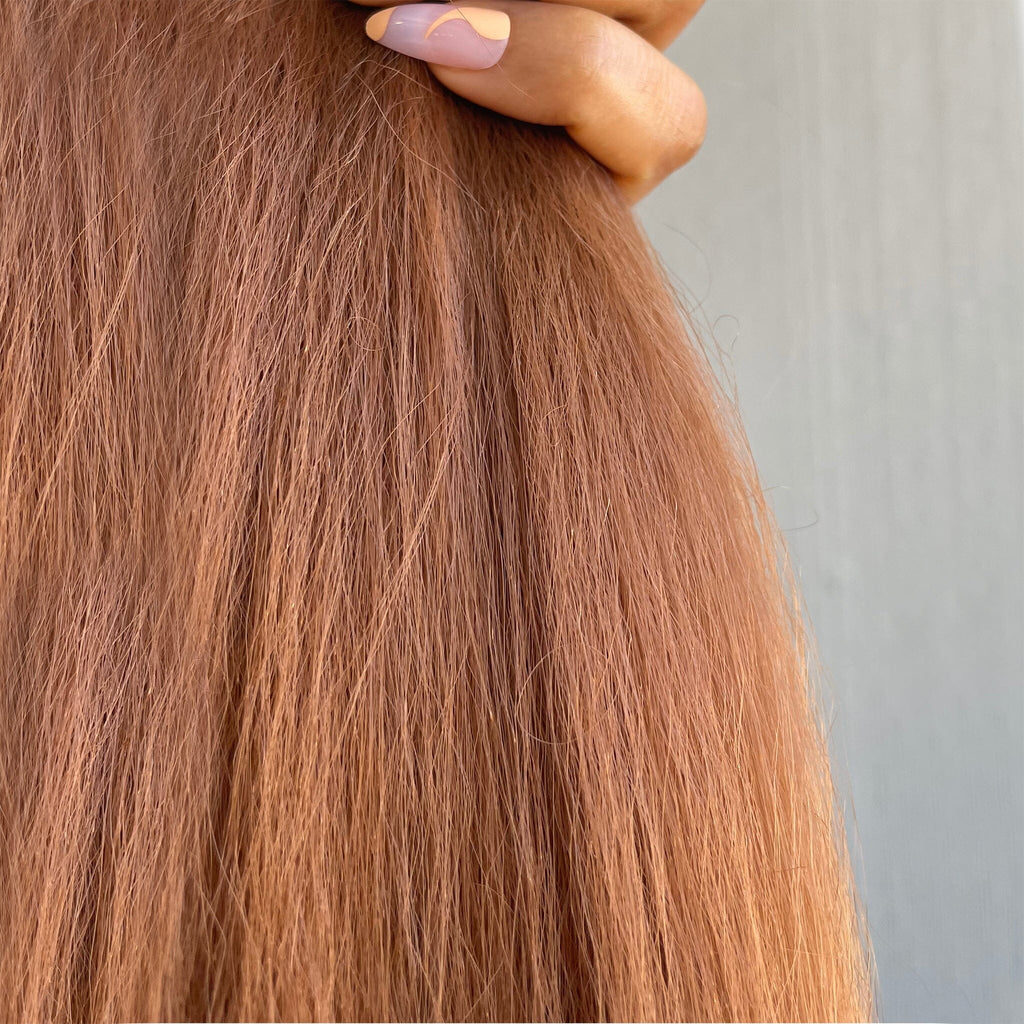 A model holds the Big Glam Nation Blowout ponytail extensions against a neutral wall. Photo gives a close up on the vibrant color and the kinkier texture of the ponytail extensions. (Red Hair Extensions/Orange Red Hair Extensions/Copper Hair Extensions).