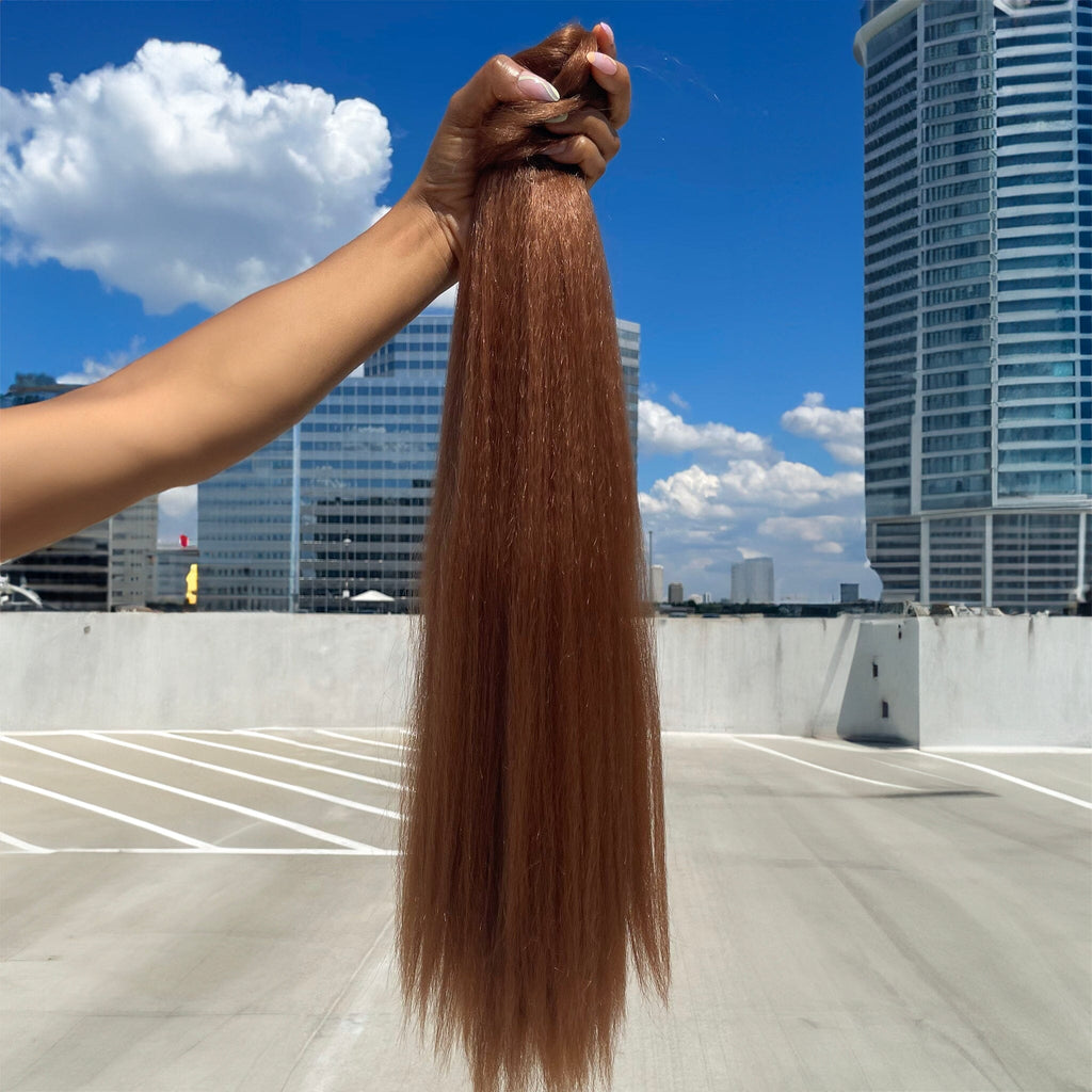 A model's hand holds the Big Glam Nation Blowout Ponytail against a sky background. The photo emphasizes the bold color, specifically - the ponytail's reddish orange hue - in sunlight. (Red Hair Extensions/Orange Red Hair Extensions/Copper Hair Extensions).