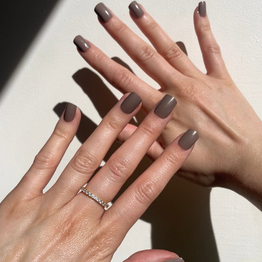 Short Press on Nails in Big Glam Nation's Burgundy and Charcoal on fair-skinned model against pale background.