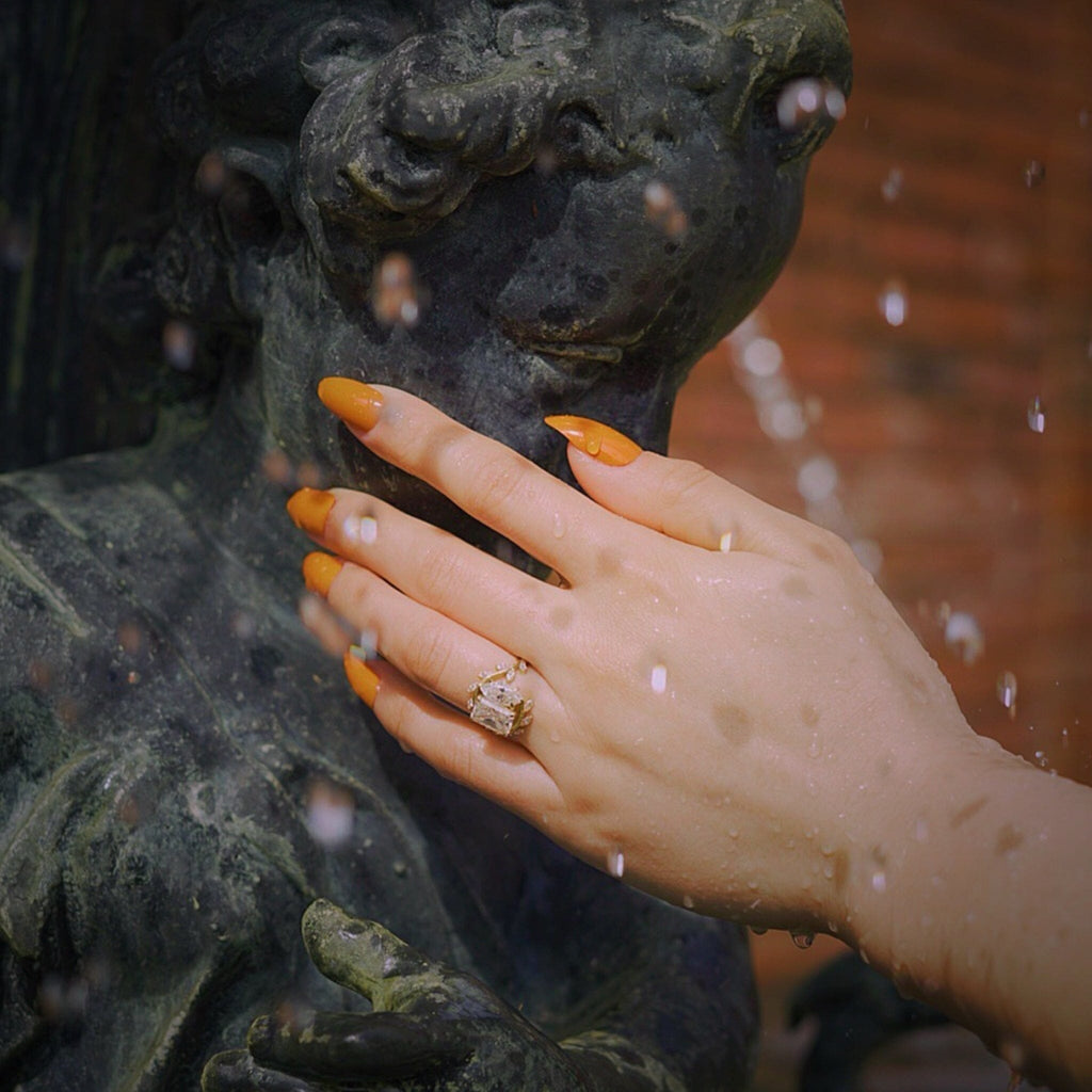 BGN's Press On Nails in ORANGE-SOLIDS worn on fair skinned models hand against scenic fountain.