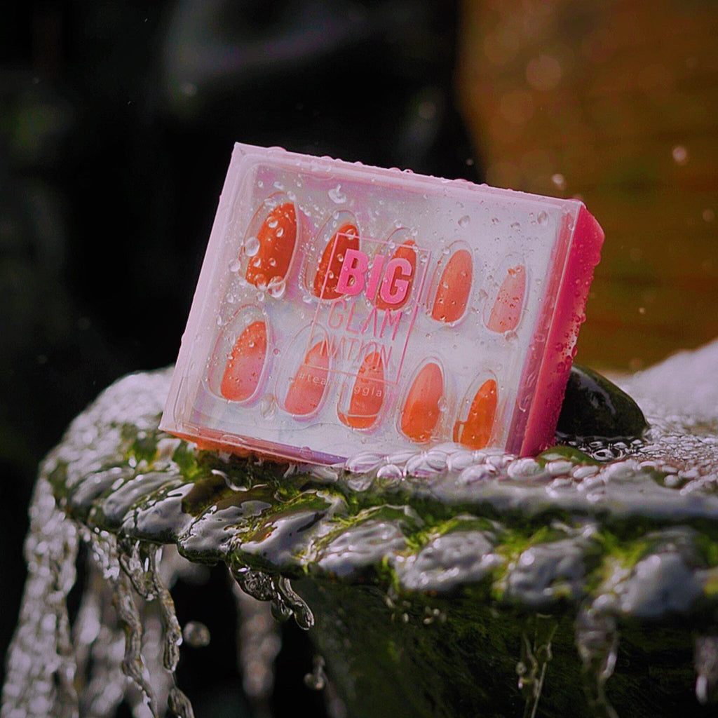 Big Glam Nation Press On Nails in bright pink packaging against water fountain