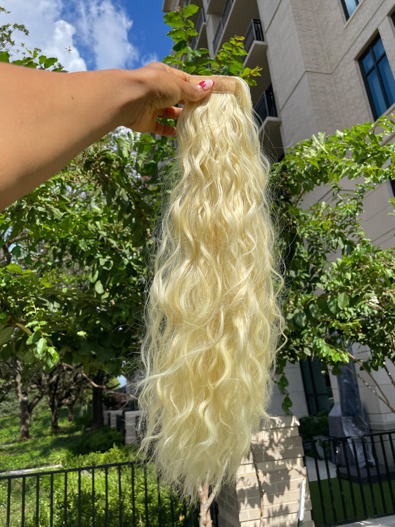 Ponytail Extensions in Big Glam Nation's Bleached Blonde are held against landscape in bright sunlight.