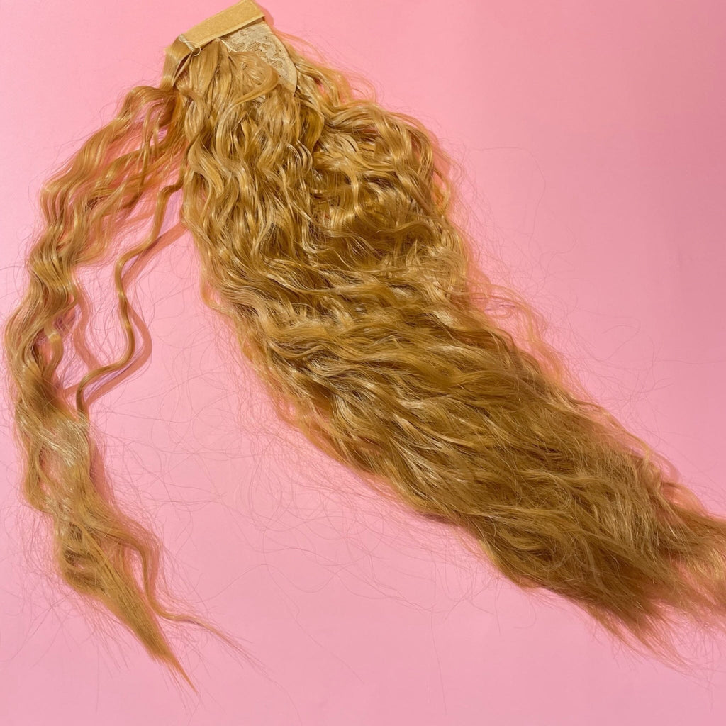 Hair Extensions in Big Glam Nation's Sandy Blonde highlight thickness perfect for thin hair while laid on warm pink background.