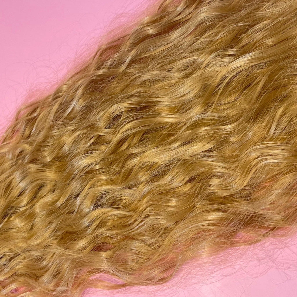 Hair Extensions in Big Glam Nation's Sandy Blonde highlight thickness perfect for thin hair while laid on warm pink background.