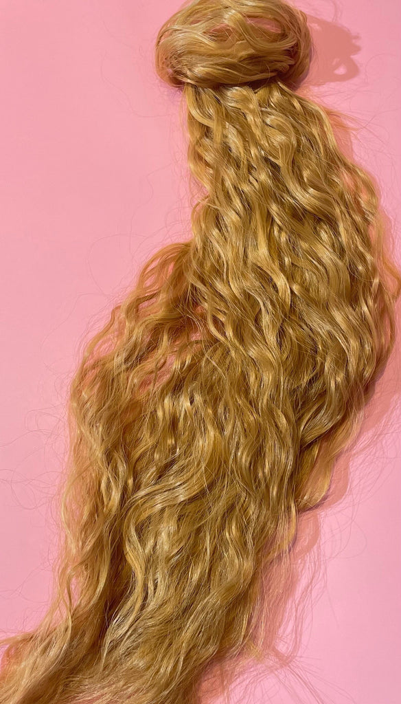 Hair Extensions in Big Glam Nation's Sandy Blonde highlight thickness perfect for thin hair while laid on warm pink background.