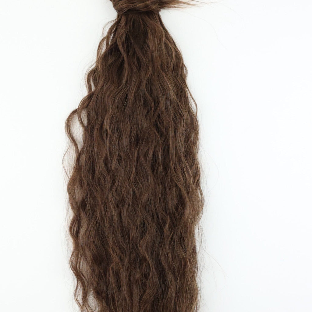 The Big Glam Nation crimped ponytail is laid flat on an off-white background. The ponytail has a wavy texture, in a sandy brown color, with a velcro wraparound application.