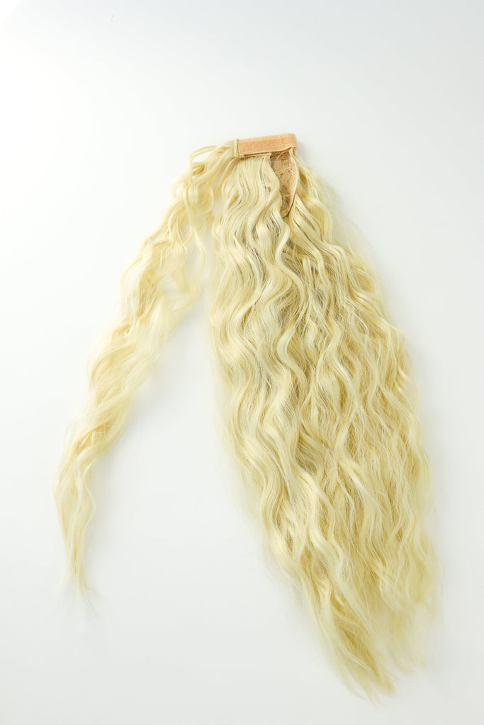 The Big Glam Nation crimped ponytail is laid flat on a white background. The ponytail has a wavy texture, in a bleach blonde color, with a velcro wraparound application.