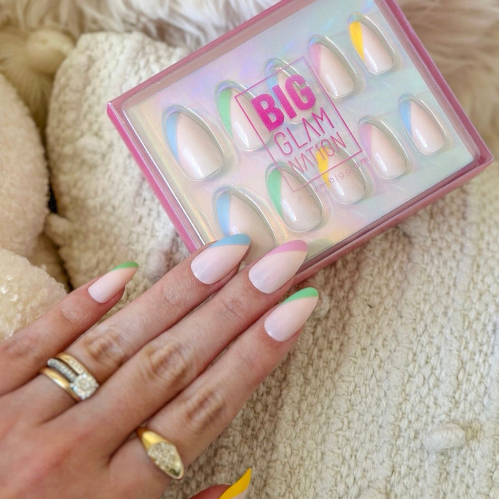 Press On Acrylic Nails in Big Glam Nation's Soft Multicolor design worn by fair-skinned model against packaging and neutral fabric.