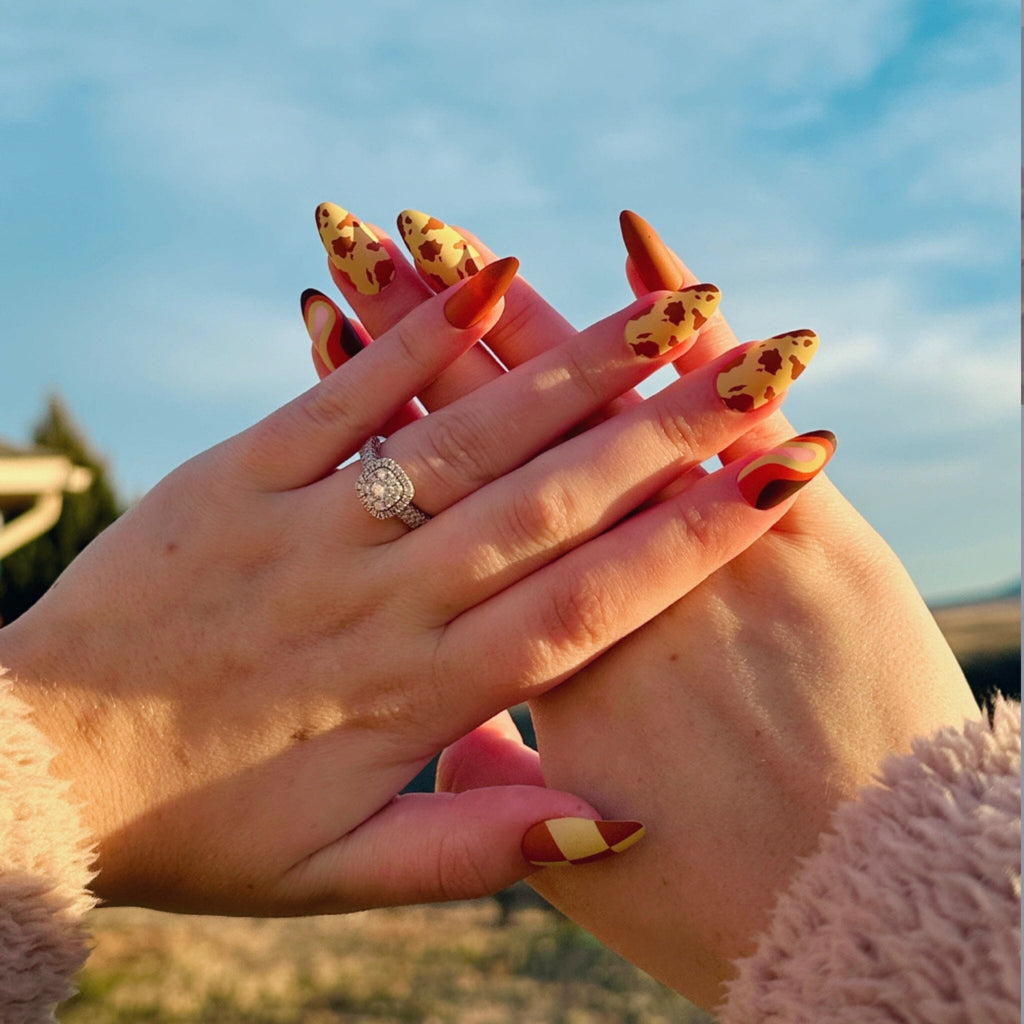 Press on Acrylic Nails in Big Glam Nation's Buttery Sherbet design worn by fair-skinned model against landscape background.