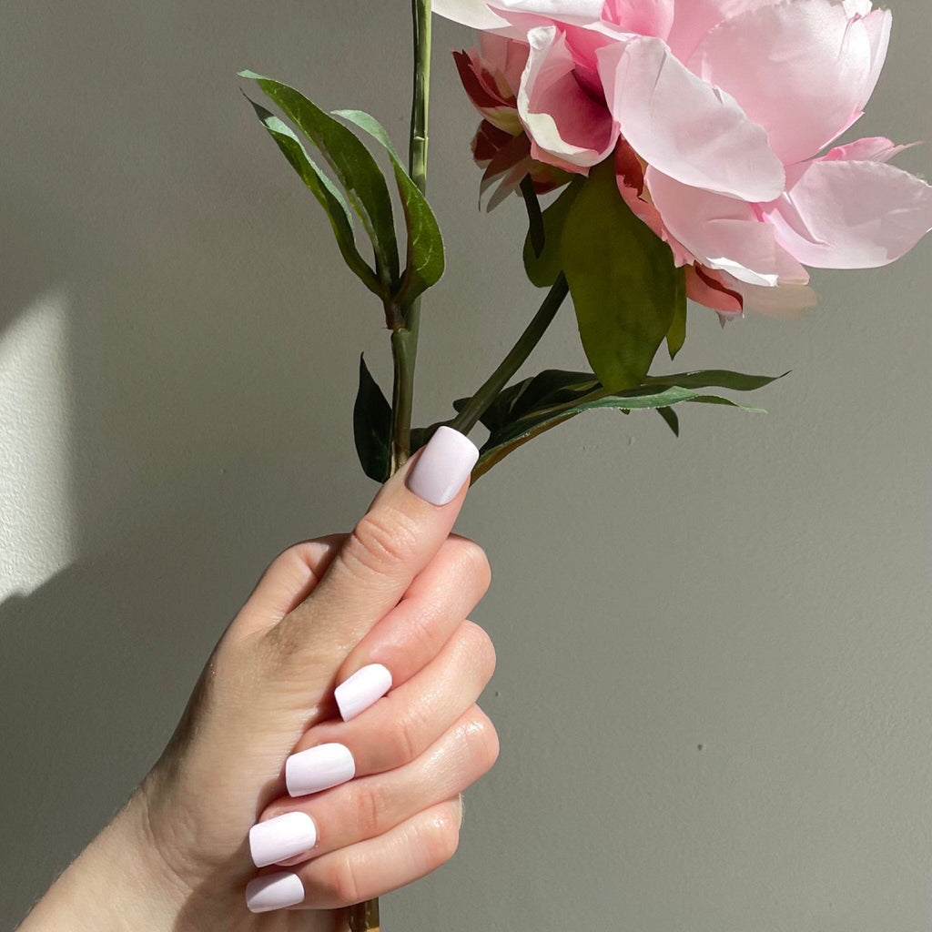 Short Press On Nails in Big Glam Natin's Soft Pink worn by fair-skinned model with flowers against pale background.