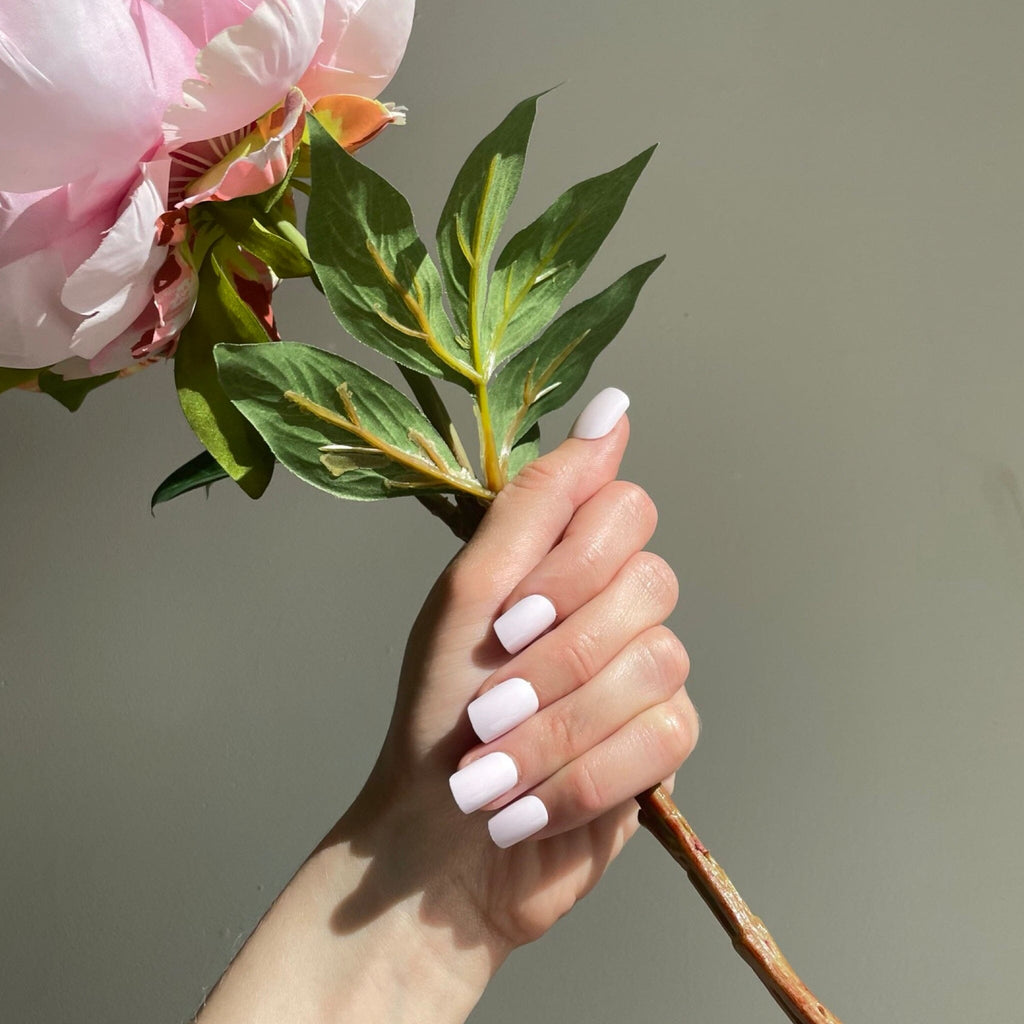 Short Press On Nails in Big Glam Natin's Soft Pink worn by fair-skinned model with flowers against pale background.