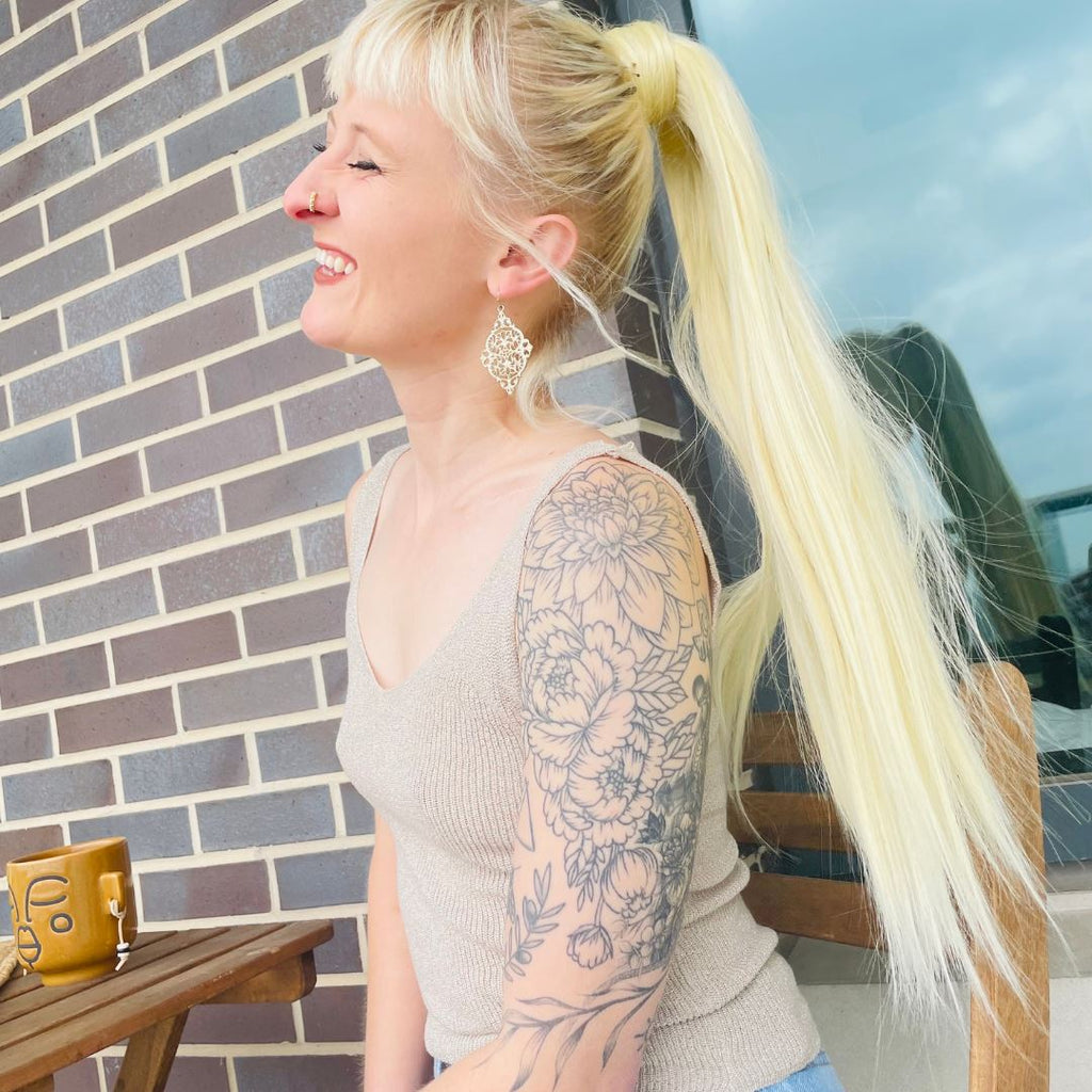 Model wearing Big Glam Nation Bleached Blonde Sleek Ponytail while sitting on an outdoor apartment balcony.